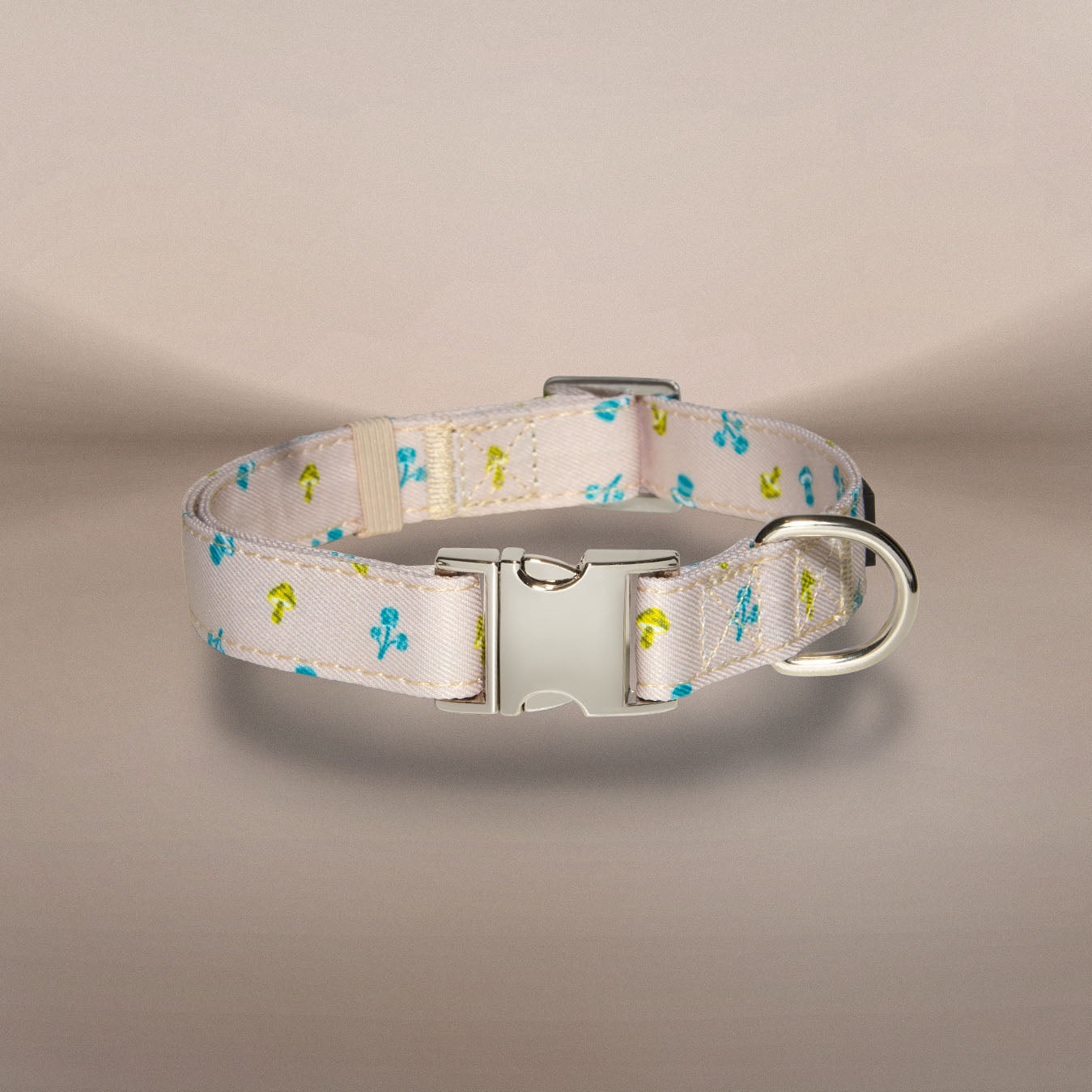 A beige dog collar with a small blue and yellow floral pattern, featuring a silver metal buckle and D-ring, displayed on a neutral beige background.